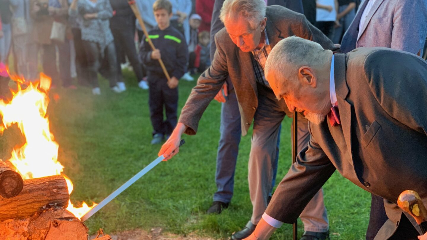 Miloš Zeman zapaluje. Hlídají ho při tom dva jeho strážci. 