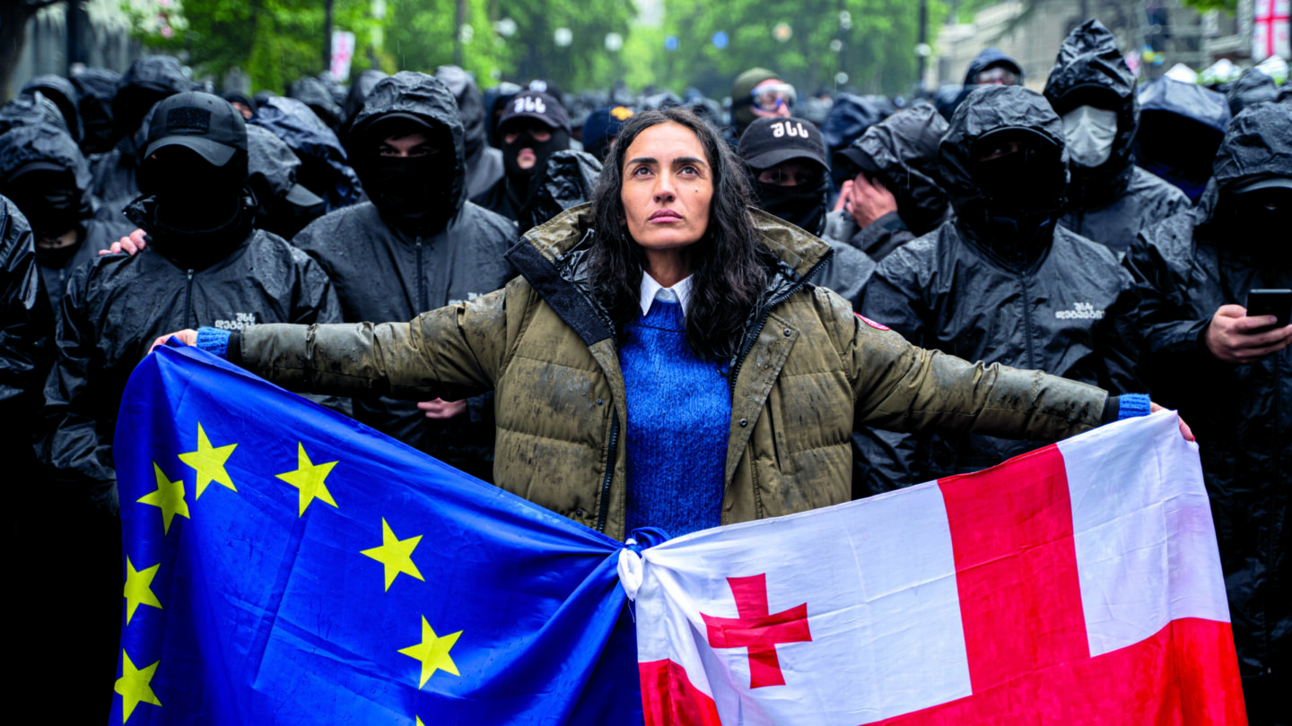 Žena drží gruzínskou vlajku a vlajku EU před kordonem maskované policie