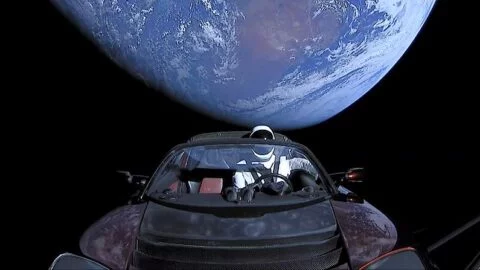 Tesla Roadster Elona Muska se Zemí v pozadí. Figurína „Starman“ ve skafandru SpaceX na místě řidiče.